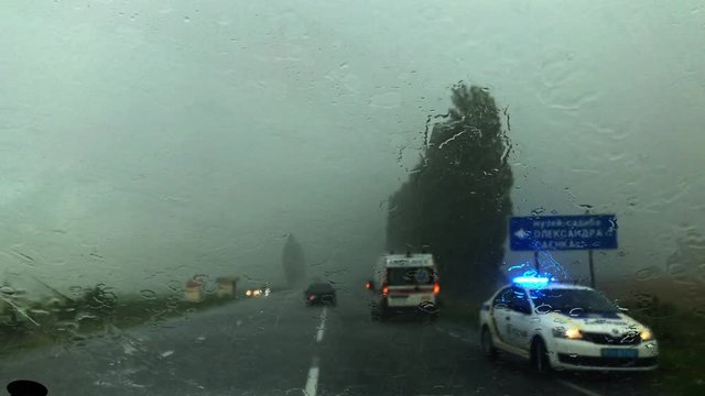 View from the front window of a car to automobile crash while rainy day. View from inside car to incident on the road while heavy rain, storm. Car's windshield wipers is working. Lights of police car