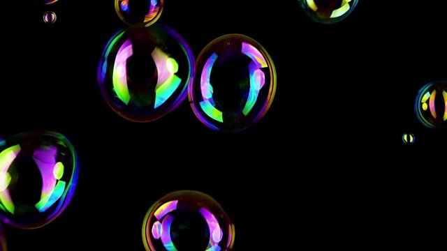 Colorful soap bubbles fly across black background. 