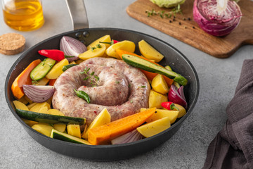 Raw sausages with potatoes, zucchini, carrots and thyme in a grill pan.