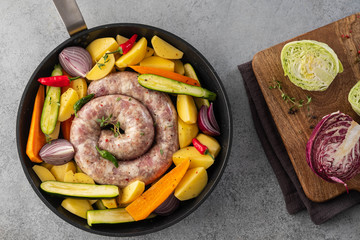 Raw sausages with potatoes, zucchini, carrots and thyme in a grill pan.