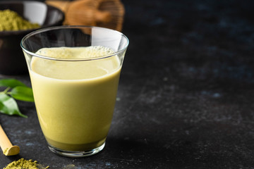 Matcha green tea latte in glass mug with whisk.