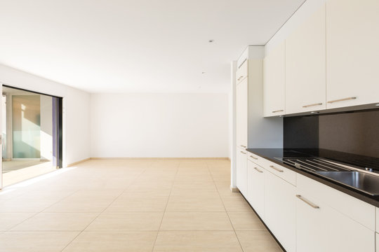 Empty Room With White Walls, Travertine Floor And White Kitchen And Black Marble