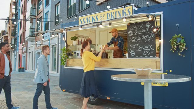 Food Truck Employee Hands Out a Freshly Made Gourmet Burgers to a Happy Young Men and Women in Queue. Street Food Truck Selling Burgers Outdoors in a Modern Hip Neighbourhood.