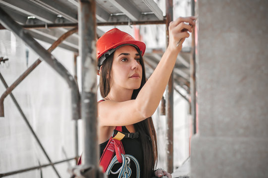 Female construction mason on the scaffolding, plastering and renovating building
