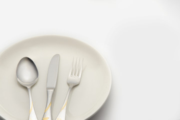 fork and spoon lay on white plate on white background