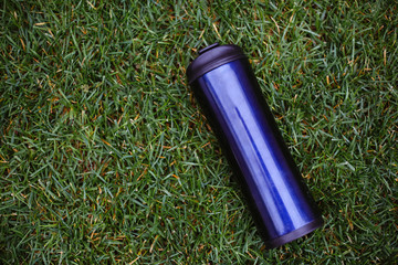 Blue stainless steel thermos, isolated on green grass.