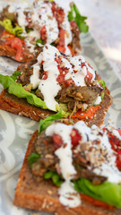 Selective focus on three slices of delicious brown bread topped with smoked aubergine, red peppers, lettuce and plant based yogurt sauce, vegetarian or vegan healthy snack served on rectangular plate