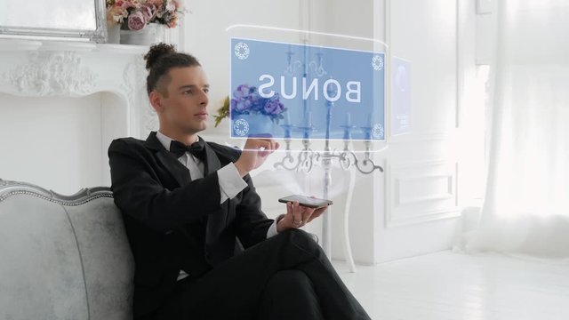 Guy businessman activates conceptual HUD hologram on smartphone with text Bonus. Young man in a white shirt and a jacket with a holographic screen on a background of the luxury room