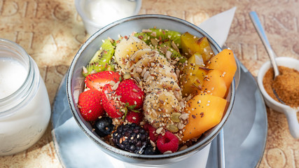 Delicious and healthy breakfast option, granola and fruit bowl featuring strawberries, bananas, kiwis, starfruit and papaya, oats, nutritious nuts and seeds, served with milk or yogurt and brown sugar