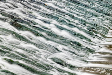 Long exposure of water flowing over algae covered rocks at Lopwell Weir, Plymouth, Devon