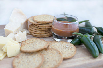 Green Chili pepper in a wooden platter with chili sauce, crackers and a variety of cheese in a white background. Close up