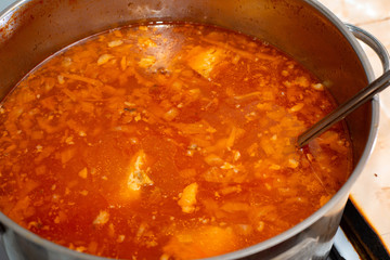 Red borsch with cabbage and fat rich meat in a pan, close-up from above.