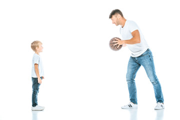happy father holding basketball and looking at cute son on white