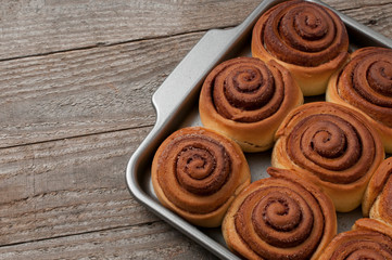Cinnamon rolls buns on a metal baking tray on wooden table