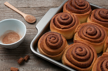 Fototapeta na wymiar Cinnamon rolls close up on a wooden table with a wood spoon and a little bowl full of sugar and cinnamon