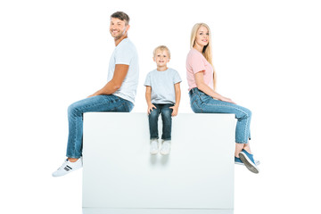 happy parents and son sitting on cube isolated on white