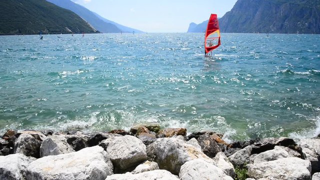 Windsurfing and paddleboarding on Lake Garda in Torbole resort. Windsurfer Surfing The Wind On Waves, Recreational Water Sports