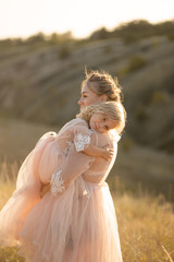 A young family in nature in identical dresses. beautiful young mom holds her daughter in her arms. Field and hills background