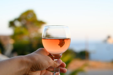 a glass of rose wine in a woman's hand against a blurred seascape