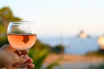 a glass of rose wine in a woman's hand against a blurred seascape