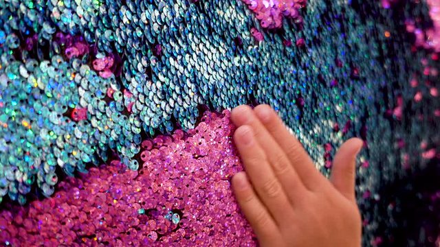 The girl's hand slowly rubbed the pink and green sequins fabric.