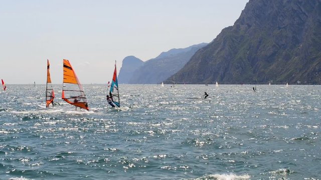 Windsurfing and paddleboarding on Lake Garda in Torbole resort. Windsurfer Surfing The Wind On Waves, Recreational Water Sports