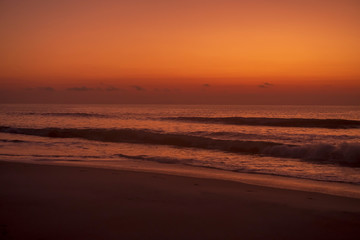 Fototapeta na wymiar The sun rising turns the sky orange over the ocean and a beach