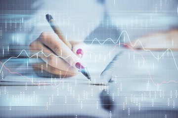 Double exposure of woman's hands making notes with forex graph hologram. Concept stock market analysis.