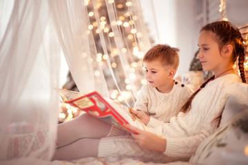 Obraz premium Brother and sister reading a book together on a cozy winter evening