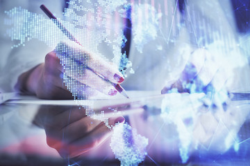 A woman hands writing information about stock market in notepad. Forex chart holograms in front. Concept of research.