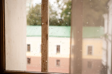 Window with raindrops. Outside the window you can see a building with a green roof, windows and a yellow-brown wall.