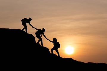 Silhouette of people helping each other hike up a mountain at sunset background. Teamwork, success and goal concept. - obrazy, fototapety, plakaty