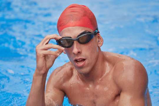 Swimmer in an outdoor pool, resting on the edge of the pool and looking at the camera, you start to take off your water goggles - Powered by Adobe