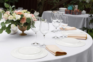 Wedding table setting decorated with fresh flowers in a brass vase. Wedding floristry. Banquet table for guests outdoors with a view of green nature. Bouquet with roses, eustoma and eucalyptus leaves