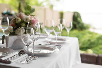Wedding table setting decorated with fresh flowers in a brass vase. Wedding floristry. Banquet table for guests outdoors with a view of green nature. Bouquet with roses, eustoma and eucalyptus leaves