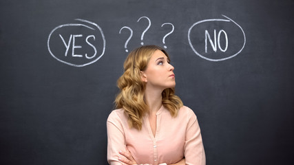 Uncertain female choosing between yes no, standing against blackboard, dilemma