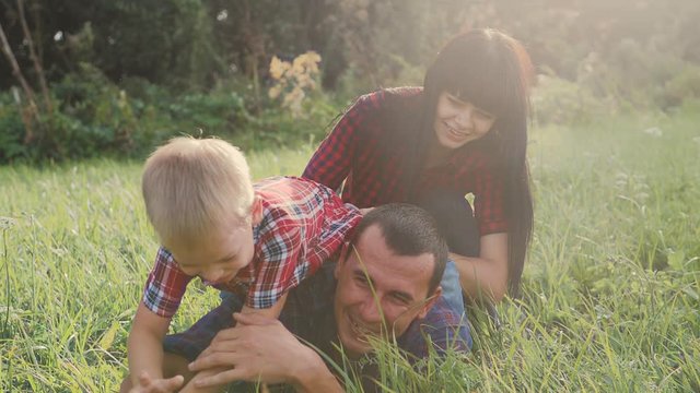 happy family teamwork outdoors have fun concept lifestyle outdoors slow motion video . mom dad and son take a photo with a smartphone in nature are sitting on the grass have fun playing .mom girl dad