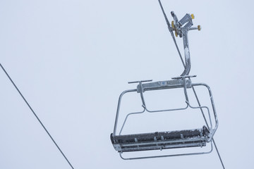 Frozen empty ski lift covered with snow on a foggy day.  Hard winter conditions, snowfall and fog.