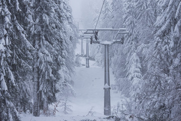 Man repairing damaged chair ski lift covered with snow on foggy snowy day. Hard winter conditions, snowfall and fog.