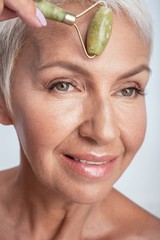 Close up of a face of aged woman rolling jade roller on her fore head