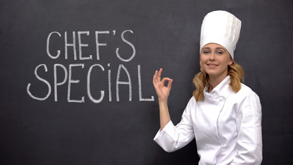 Female senior cook showing ok sign against background with chiefs special phrase
