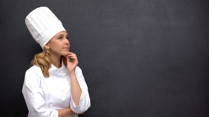 Pensive senior cook touching chin against black board, searching for inspiration