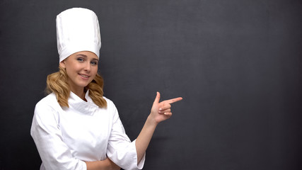 Smiling senior cook pointing finger into blackboard, cafe, template for text