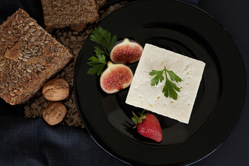 White luxury expensive cheese, decorated with figs and strawberries, on a black plate, next to bread and cereals and walnuts. The concept of useful natural products or cheese products.