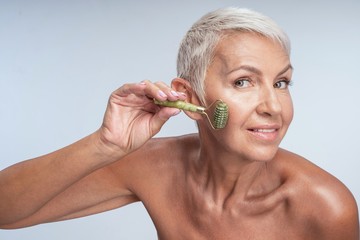 Beautiful mature lady looking into the camera while rolling the jade roller on her face