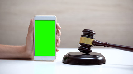 Female hand holding smartphone green screen, gavel standing on sound block, app