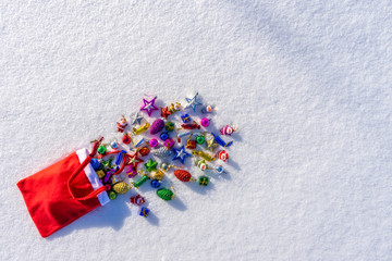 Red bag with many colorful new year toys lying on white fresh snow. Santa Claus scattered bag of gifts. Merry Christmas and Happy New Year. Greeting card for winter holidays. Top view, copy space