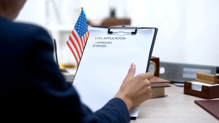 Female immigration inspector denying visa application, american flag on table