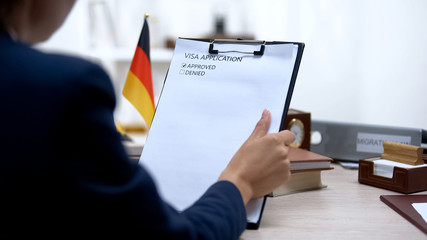 Embassy employee approving visa application, german flag on table, authority