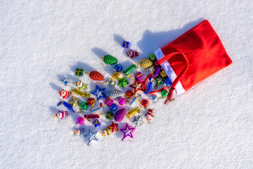 Red bag with many colorful new year toys lying on white fresh snow. Santa Claus scattered bag of gifts. Merry Christmas and Happy New Year. Greeting card for winter holidays. Top view, copy space